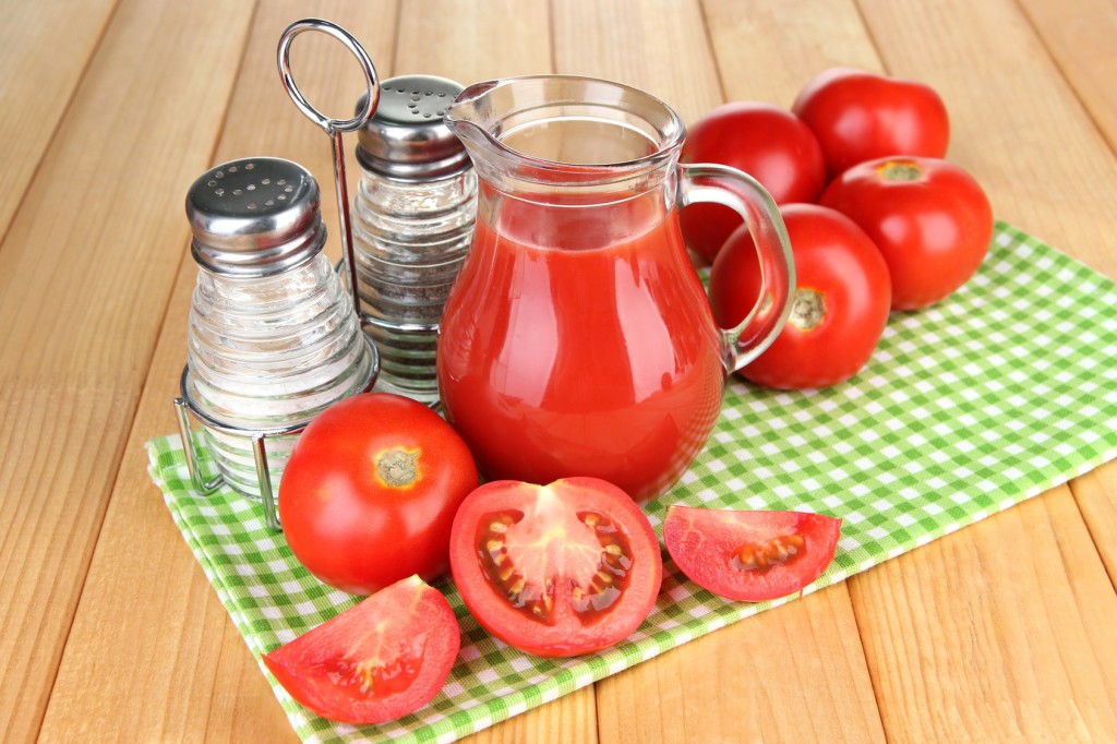 Tomato juice in glass jug, on wooden background