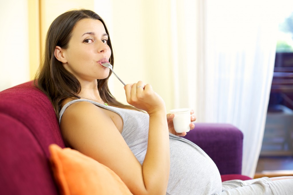 Happy pregnant woman licking spoong with yogurt
