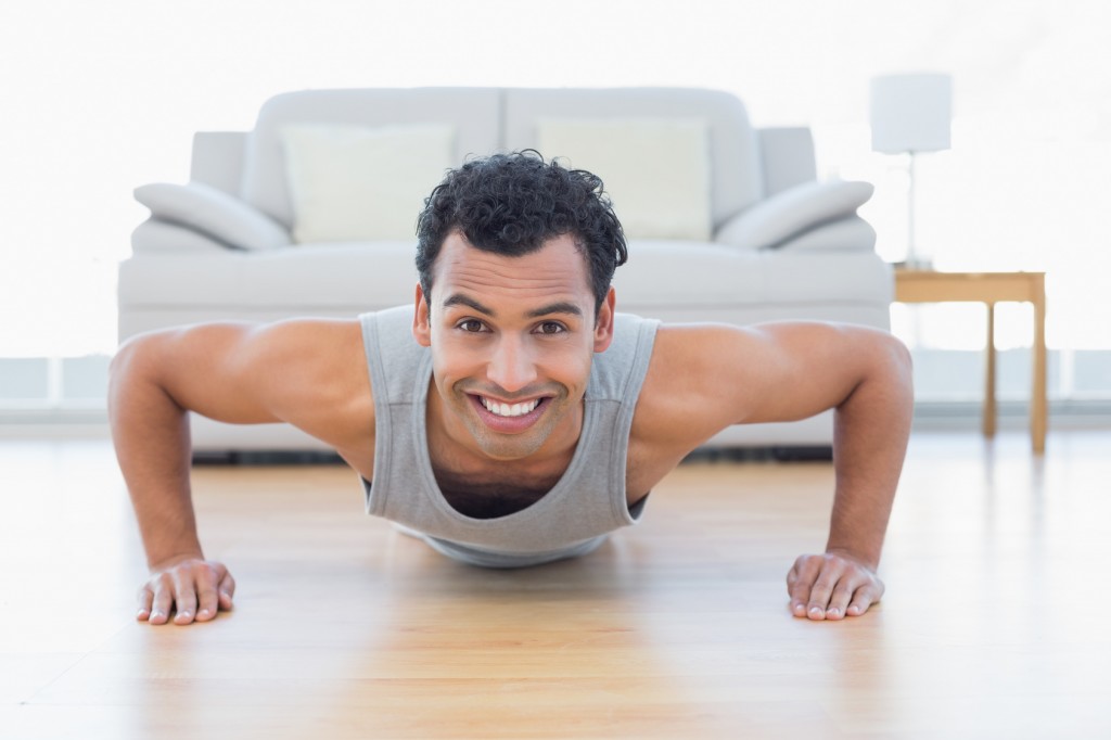 Portrait of a sporty smiling young man doing push ups in the living room at house