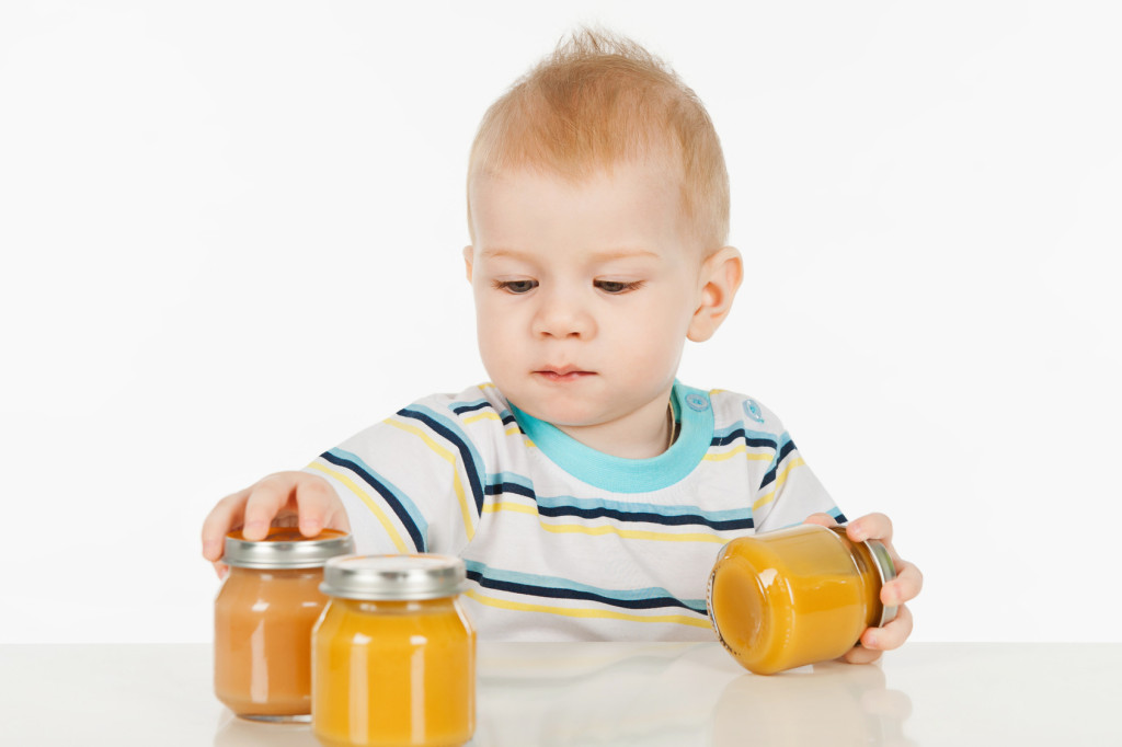 Boy with little jars of baby food, on a gray background