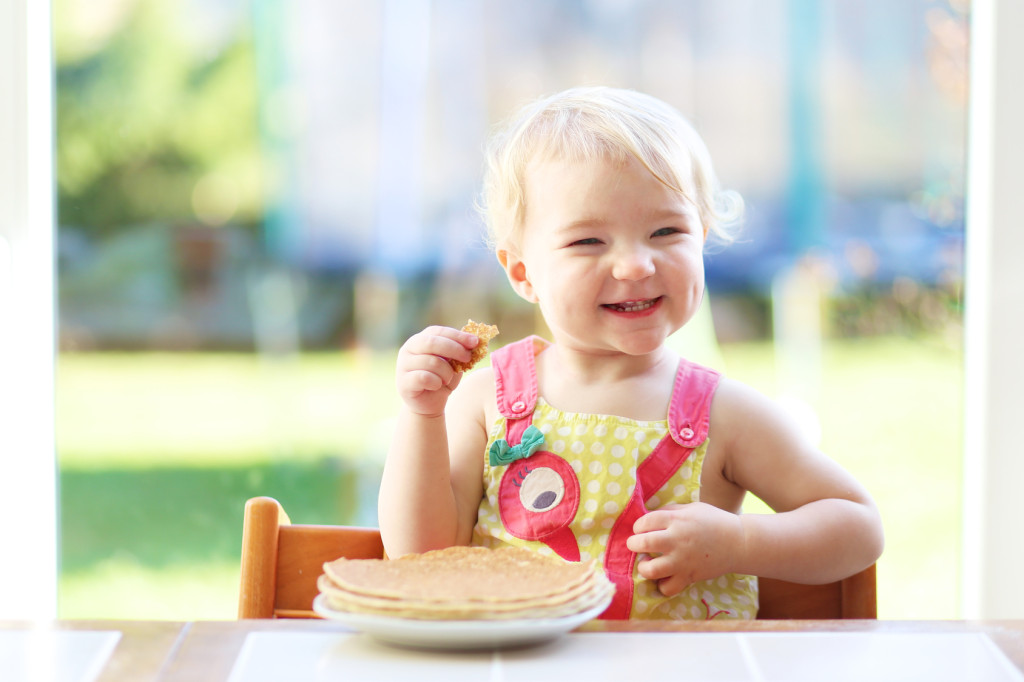 Happy little toddler girl eating delicious pancakes