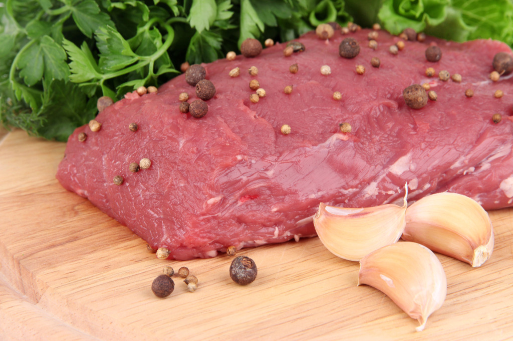 Raw beef meat with spices and greens on wooden background