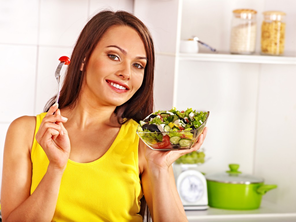 Woman eating salad at kitchen.