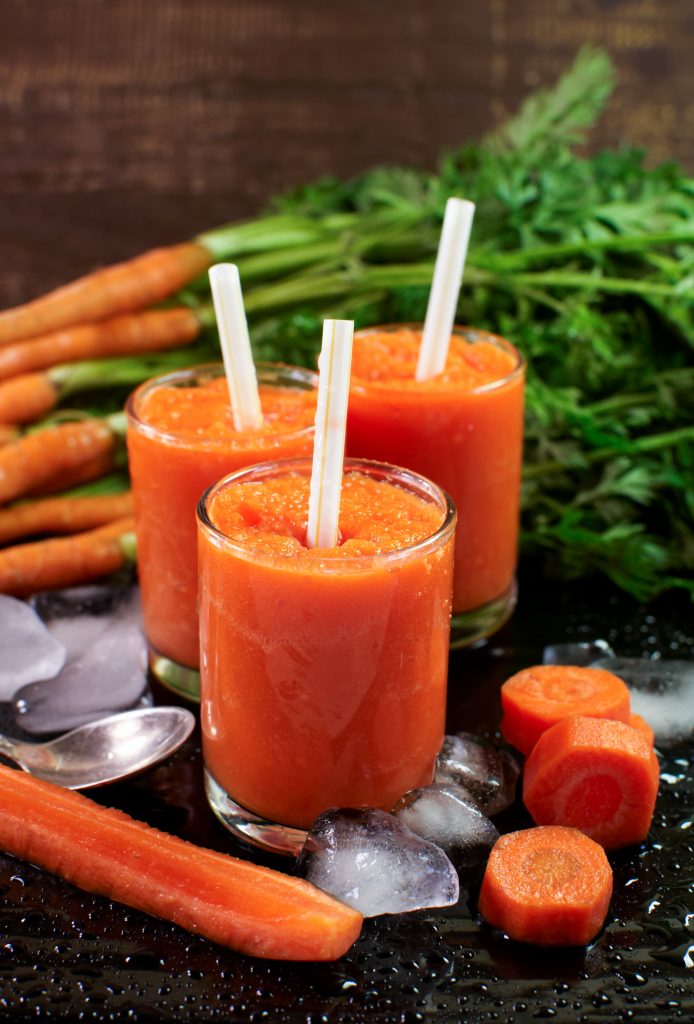 Glasses with carrot smoothies. Fresh carrot on a wooden surface.